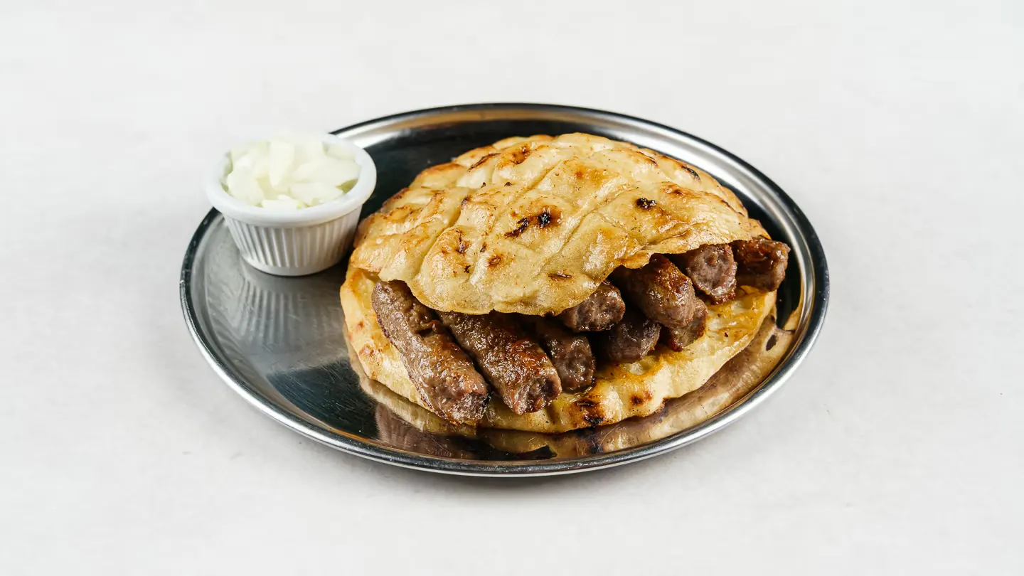 Ćevapi sa somunom i lukom posluženi na tanjuru u restoranu Baščaršija u Zagrebu